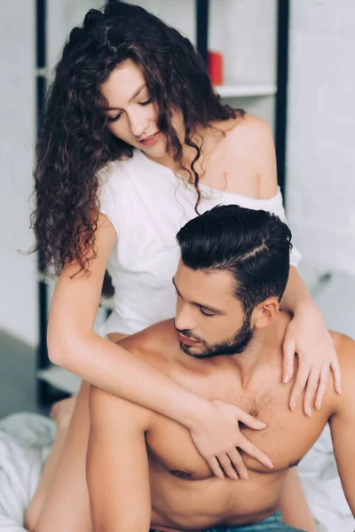 Sorridente menina abraçando sem camisa muscular namorado no quarto em casa — Fotografia de Stock