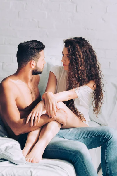 Attractive curly girl sitting on boyfriend knees on bed in morning at home — Stock Photo