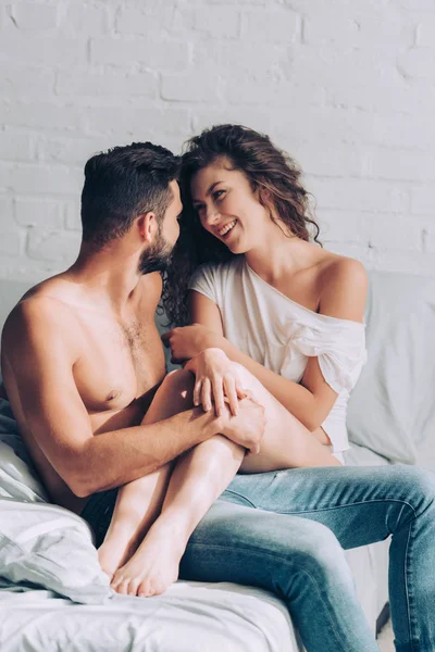 Riendo joven rizado mujer sentado en novio rodillas en dormitorio en casa - foto de stock