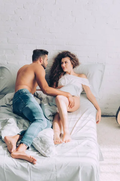 Високий кут зору без сорочки м'язистий чоловік в джинсах торкається молодої сексуальної дівчини на ліжку вдома — стокове фото