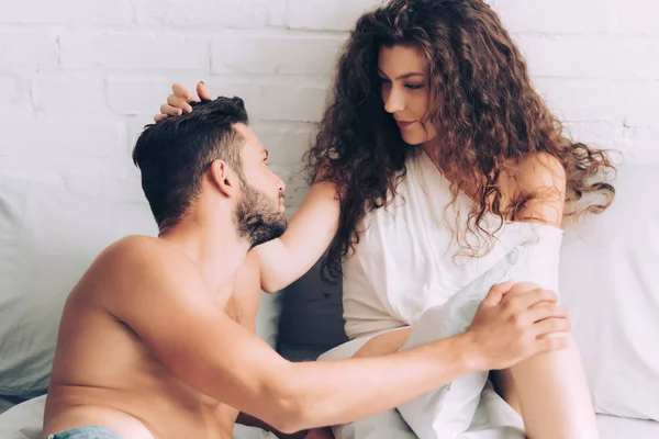 Smiling curly woman touching hair of boyfriend in bedroom at home — Stock Photo