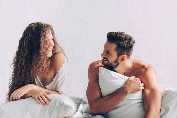 Rindo jovem casal deitado na cama com travesseiros no quarto em casa — Fotografia de Stock