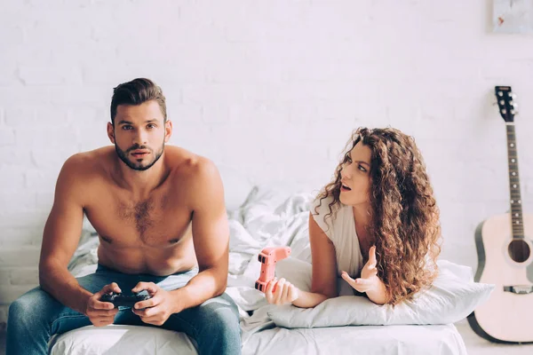 Irritado jovem mulher gestos à mão enquanto seu namorado concentrado jogar vídeo game por joystick — Fotografia de Stock