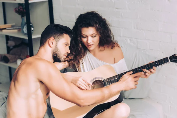 Високий кут зору без сорочки чоловік навчає красиву дівчину грати на акустичній гітарі в спальні вдома — стокове фото