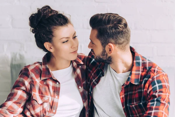 Joyeuse jeune femme en chemise à carreaux embrassant petit ami à la maison — Photo de stock