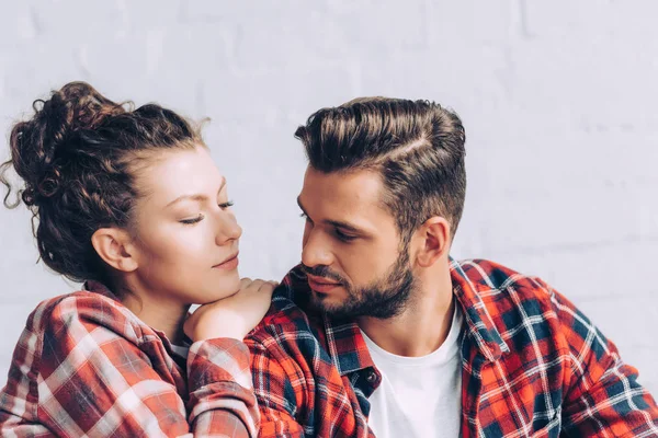 Bonita mujer joven en camisa a cuadros abrazando novio en casa - foto de stock