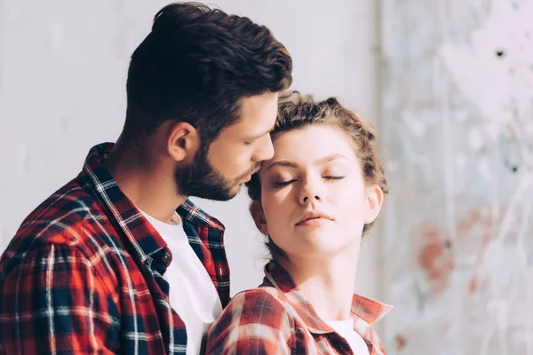 Selective focus of man in checkered shirt hugging girlfriend at home — Stock Photo
