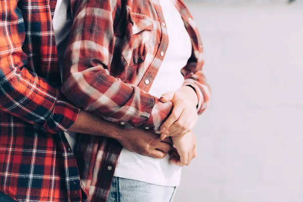 Cropped image of man in checkered shirt hugging girlfriend from behind at home — Stock Photo