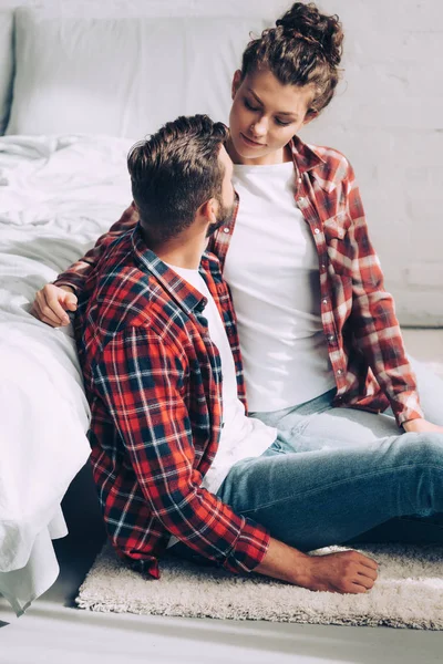 Junges Paar in karierten Hemden, das auf dem Boden sitzt und sich zu Hause im Schlafzimmer anschaut — Stockfoto