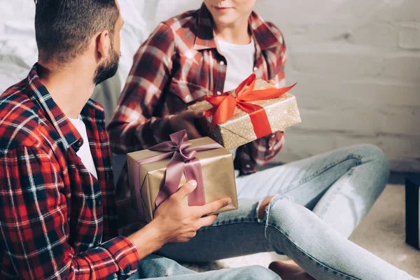 Image recadrée de couple en chemises à carreaux donnant cadeaux de Noël les uns aux autres à la maison — Photo de stock
