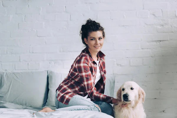 Smiling young woman petting golden retriever in bedroom at home — Stock Photo