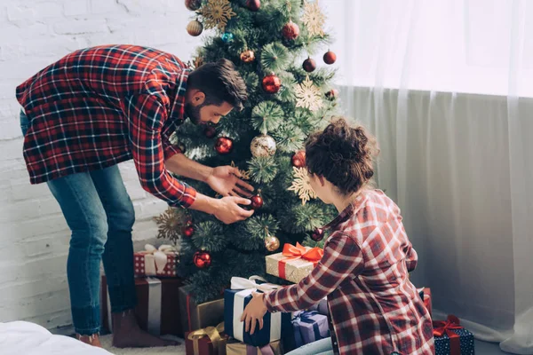Paar in karierten Hemden schmückt Weihnachtsbaum zu Hause — Stockfoto