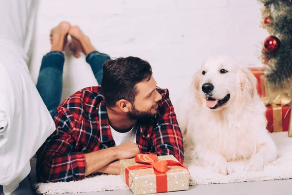 Jovem alegre com adorável golden retriever no Natal em casa — Fotografia de Stock