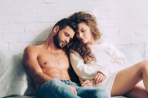Ricci attraente ragazza seduta con bel fidanzato senza maglietta in camera da letto a casa — Foto stock
