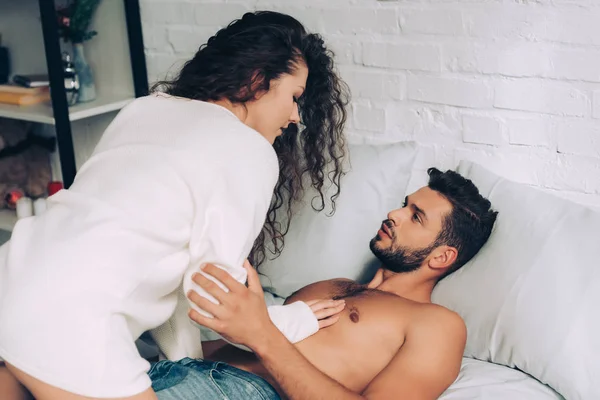 Vista ad alto angolo di ragazza riccia seduta su uomo muscoloso senza maglietta in camera da letto a casa — Foto stock
