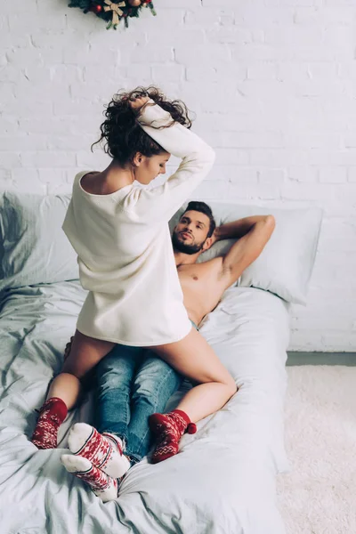 Вид ззаду спокуслива кучерява жінка сидить на сорочці хлопця на ліжку вдома — стокове фото