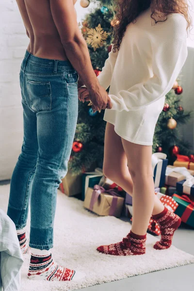 Cropped image of couple holding hands of each other near christmas tree at home — Stock Photo