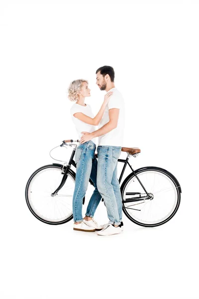 Привлекательная пара обнимается, стоя возле велосипеда, изолированного на белом — стоковое фото