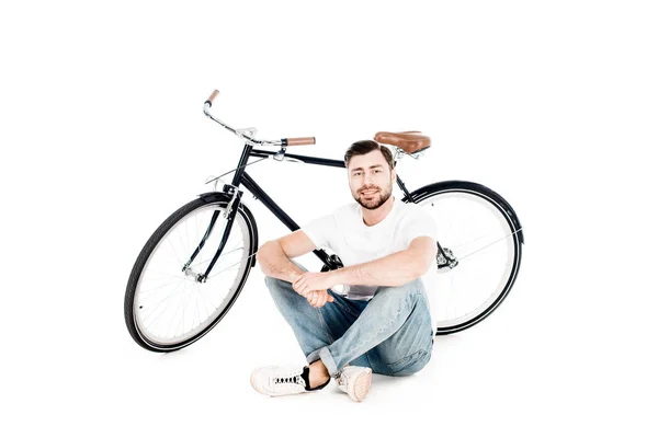 Bello sorridente giovane adulto seduto vicino alla bicicletta isolato su bianco — Foto stock