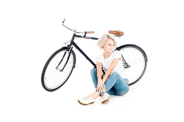 Wonderful blonde young adult woman sitting near the bicycle isolated on white — Stock Photo