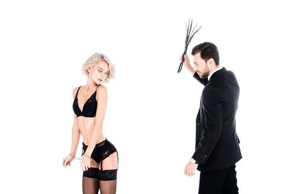 Seductive beautiful woman standing in wonderful lingerie while man raising his hand with whip isolated on white — Stock Photo