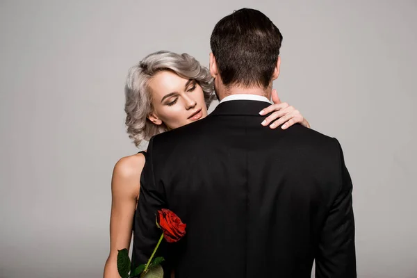 Pareja de adultos jóvenes abrazándose mientras mujer sosteniendo rosa roja - foto de stock