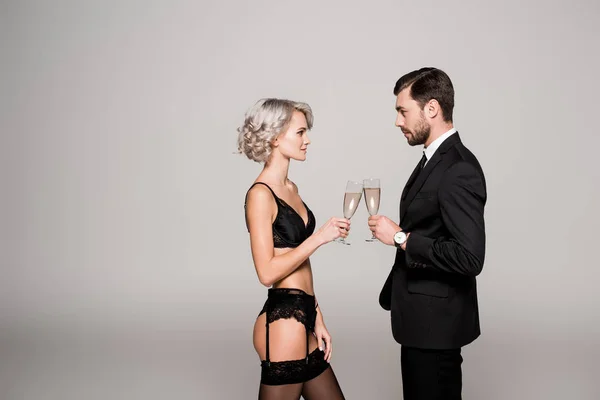 Привлекательная пара звон бокалов шампанского в то время как женщина находится в красивом белье изолированы на сером — стоковое фото