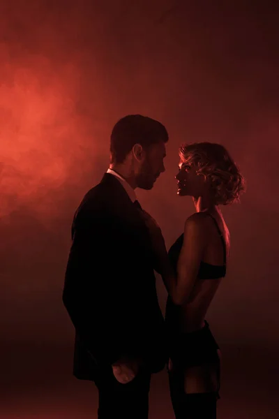 Couple attrayant de jeunes adultes se regardant amoureusement sur fond de fumée rouge — Photo de stock