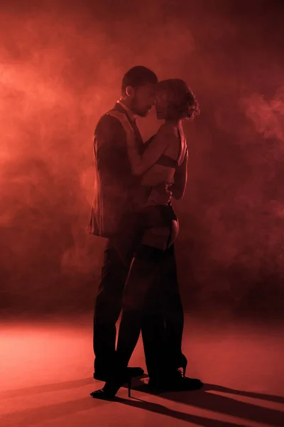 Beau couple câlin et presque embrasser sur fond de fumée rouge — Photo de stock