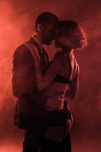 Maravillosa pareja abrazándose en el fondo de humo rojo - foto de stock