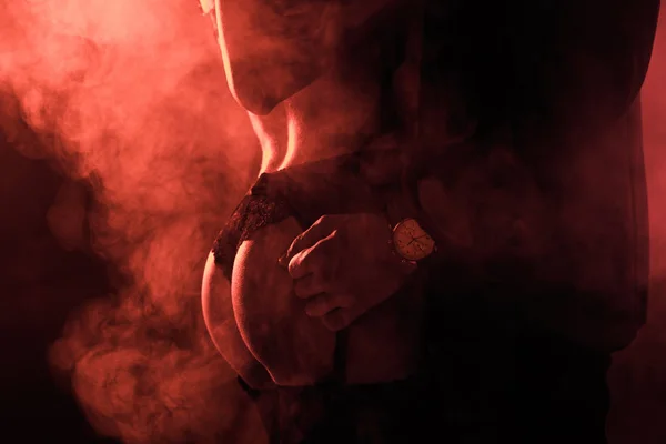 Vista parcial de pareja seductora apasionada en abrazo sobre fondo de humo rojo - foto de stock