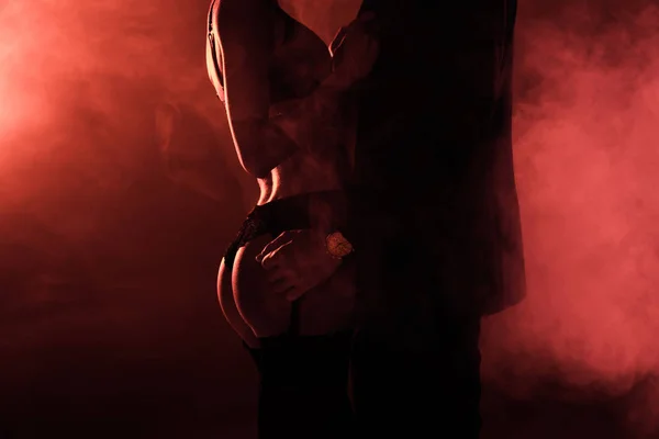Vista parcial de atractiva pareja seductora en abrazo sobre fondo de humo rojo - foto de stock
