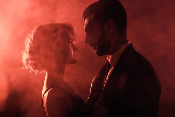 Schönes Paar, das sich auf rotem Rauch-Hintergrund amourös ansieht — Stockfoto