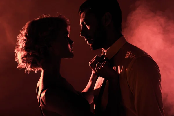 Beautiful couple of young adults looking at each other on red smoke background — Stock Photo