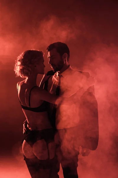 Attraktives Paar umarmt sich auf rotem Rauch-Hintergrund — Stockfoto