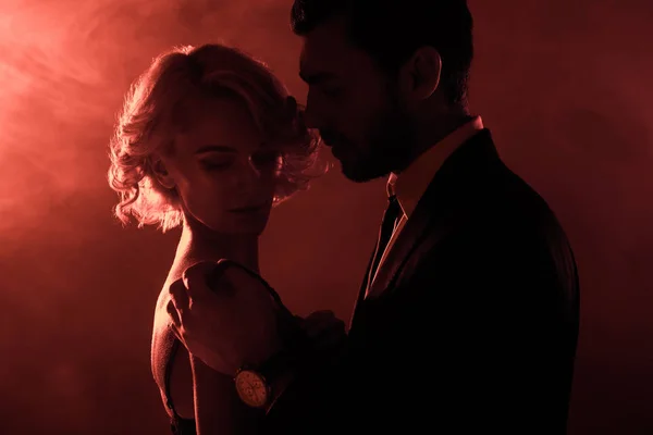 Leidenschaftliches Paar umarmt sich auf rotem Rauch-Hintergrund — Stockfoto
