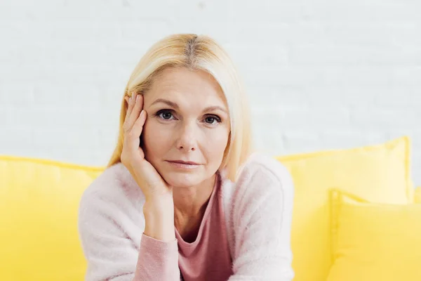 Close up of beautiful blonde mature woman sitting on bright yellow sofa — Stock Photo