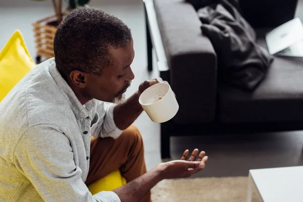 Mature african american man sitting on sofa and drinking coffee in living room — Stock Photo