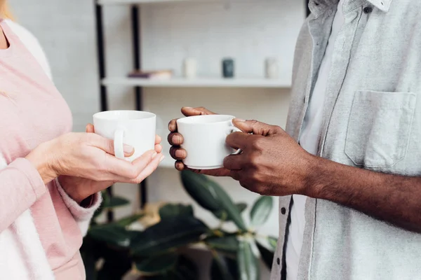 Close up of woman and african american man holding white cups — Stock Photo