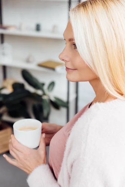 Attraente sorridente donna bionda matura in possesso di tazza di caffè bianco — Foto stock