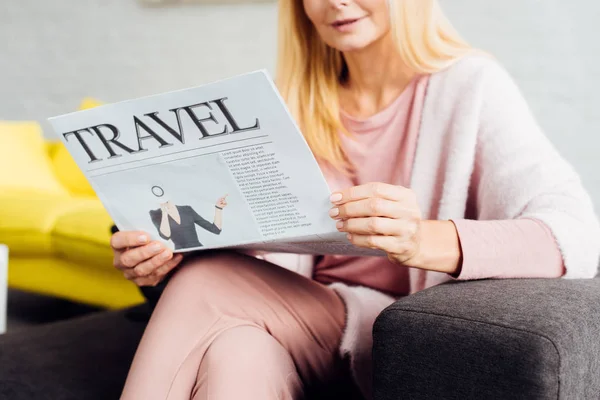 Close up de mulher madura sentada no sofá e lendo jornal de viagem — Fotografia de Stock