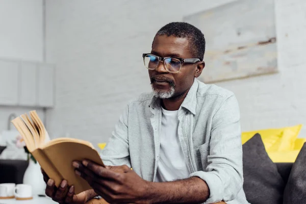 Africano americano maduro hombre en gafas lectura libro - foto de stock