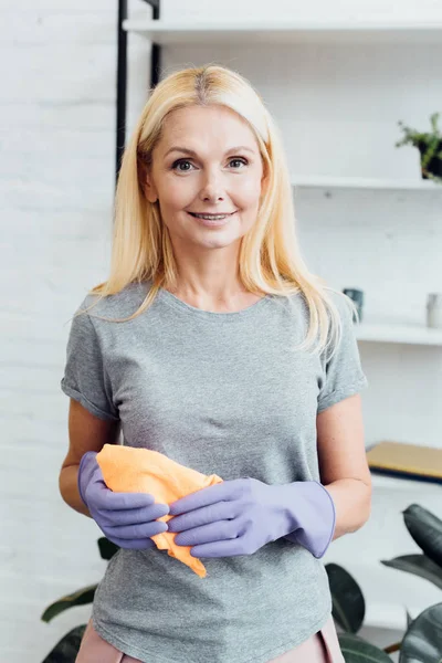 Sonriente mujer madura en guantes de goma sosteniendo tela - foto de stock