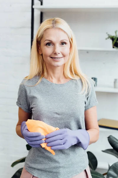 Sorrindo mulher madura em luvas de borracha segurando pano — Fotografia de Stock