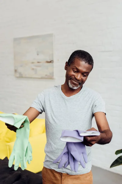 Guapo sonriente afroamericano hombre sosteniendo guantes de goma - foto de stock