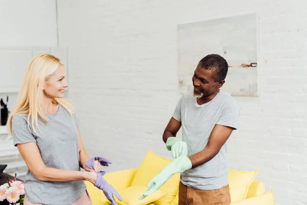 Happy african american man and blonde mature woman putting on rubber gloves — Stock Photo