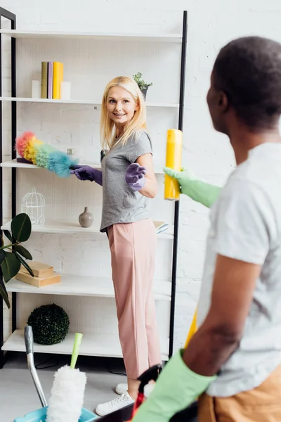 Blonde souriante femme avec plumeau à la main prenant pulvérisation jaune — Photo de stock