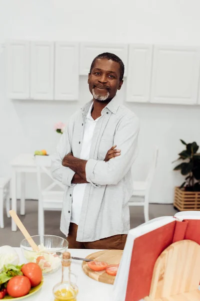 Hombre afroamericano de pie con los brazos cruzados en la cocina - foto de stock