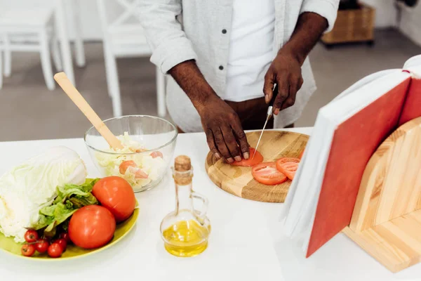 Uomo africano americano affettare pomodori su tagliere di legno — Foto stock