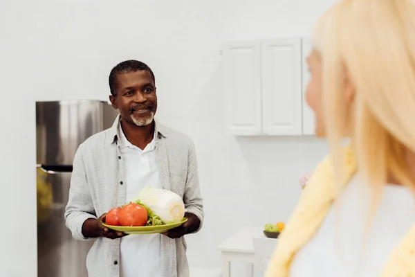 Hombre afroamericano sosteniendo verduras y mirando a la mujer - foto de stock